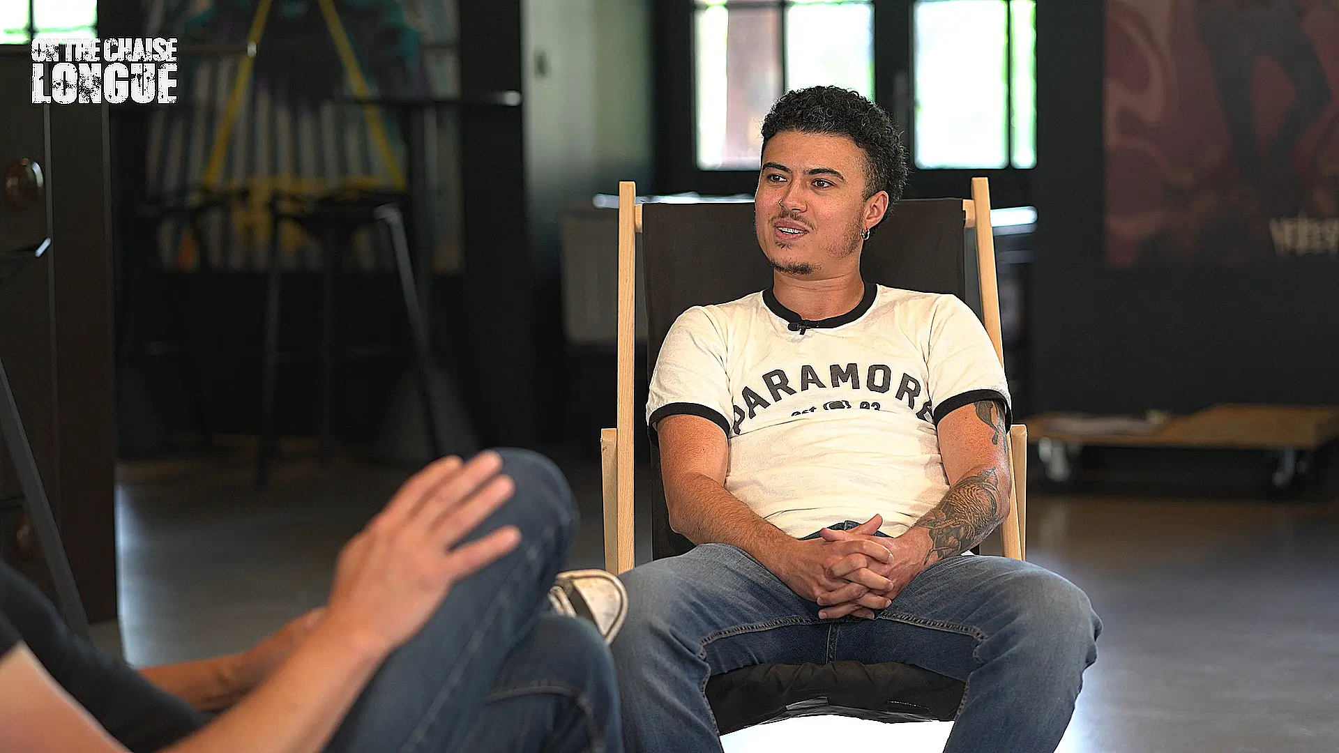 Le chanteur du groupe Stinky, vêtu d’un t-shirt Paramore, assis sur une chaise longue lors d’une interview dans les locaux du Hellfest, discutant dans une ambiance décontractée.